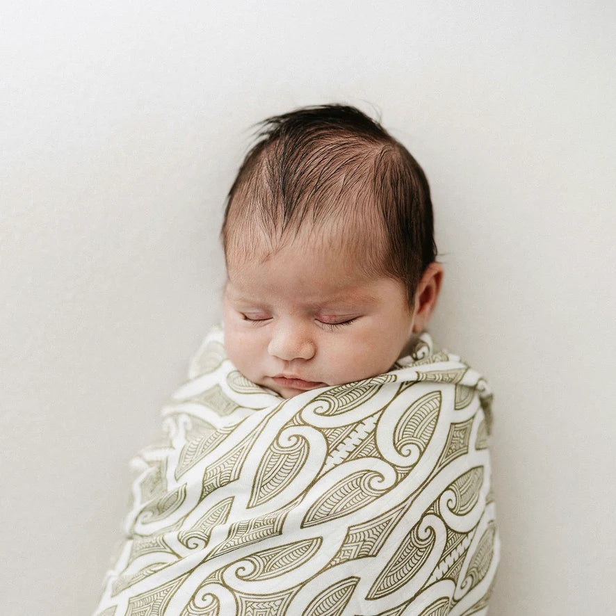 Sleeping baby wrapped in a patterned linen swaddle against white background