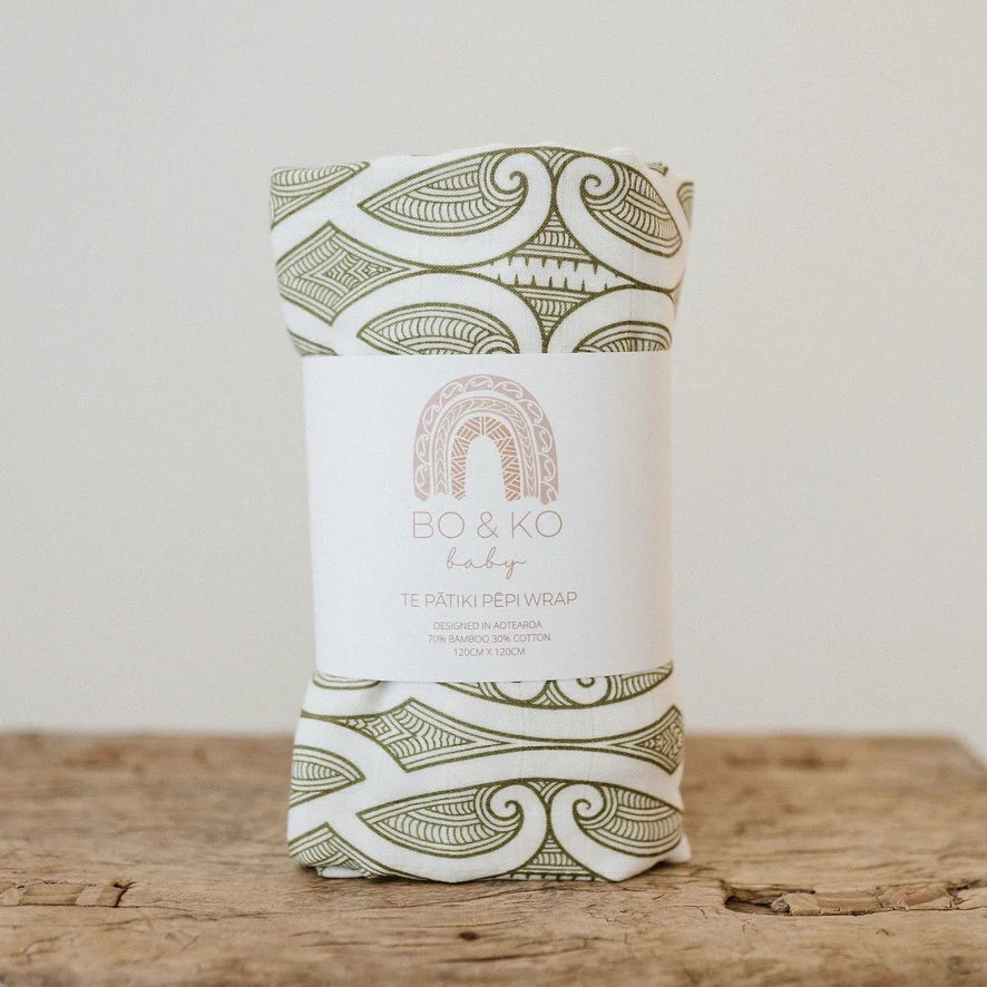 Patterned bamboo cotton baby wrap in green and white on rustic wood surface