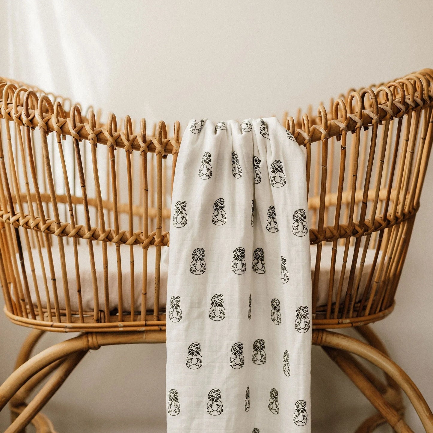 White linen blanket with black pattern draped over a natural rattan bassinet