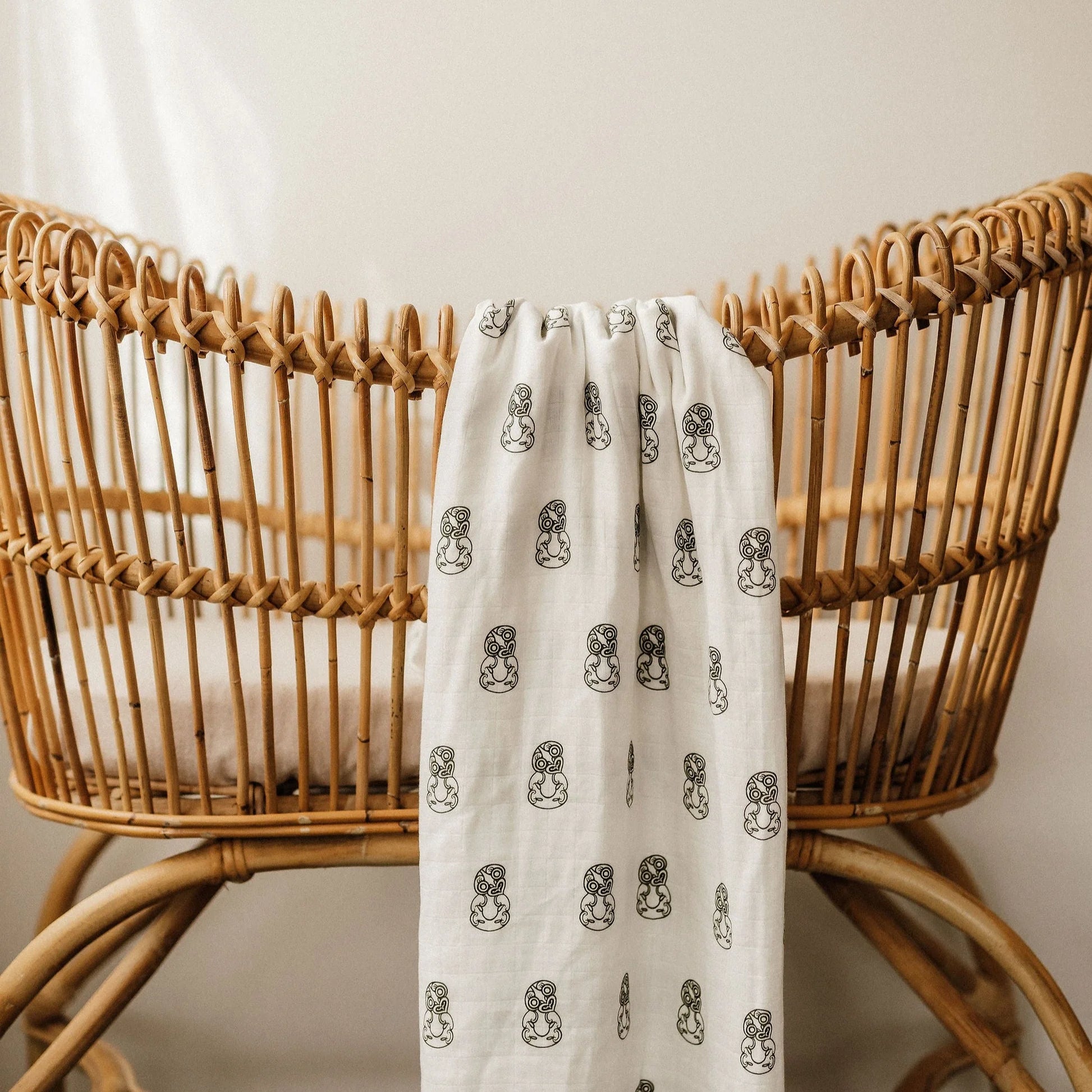 White linen blanket with black pattern draped over a natural rattan bassinet