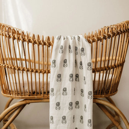 White linen blanket with black pattern draped over a natural rattan bassinet