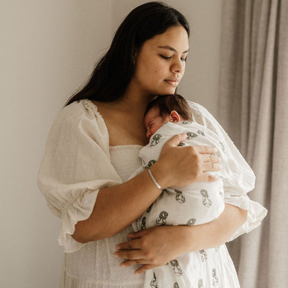 Woman in a white linen dress gently holding a newborn swaddled in a patterned linen blanket