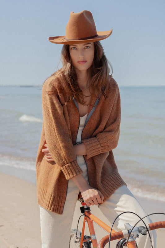 Woman sitting on a bike wearing rust hooded cardigan with zip front and cable back.
