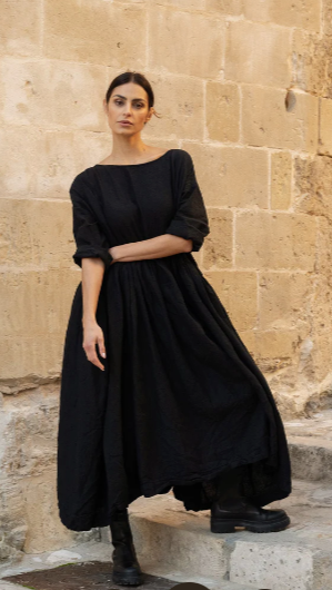 Woman wearing black linen maxi dress with sleeves and pockets. Worn front and back.