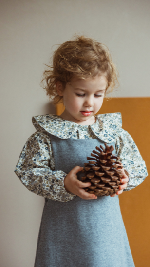 Child wearing floral long sleeve shirt with button front under a pinafore dress.