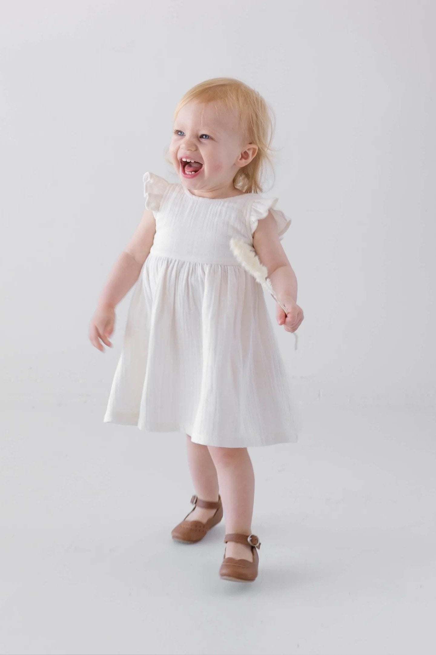 toddler wearing white ruffle sleeve dress with bow tie back front view