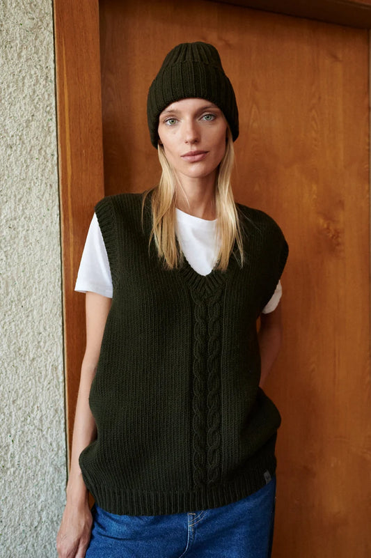 Woman wearing a khaki cashmere vest with a cable pattern down the front.