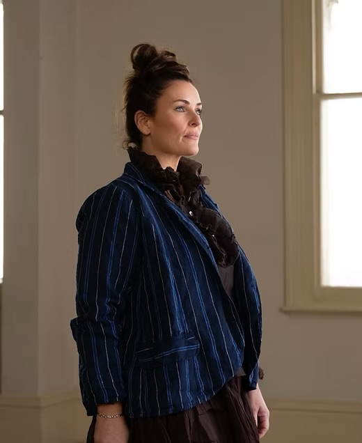 Woman wearing a blue pinstripe linen jacket and brown ruffle blouse indoors