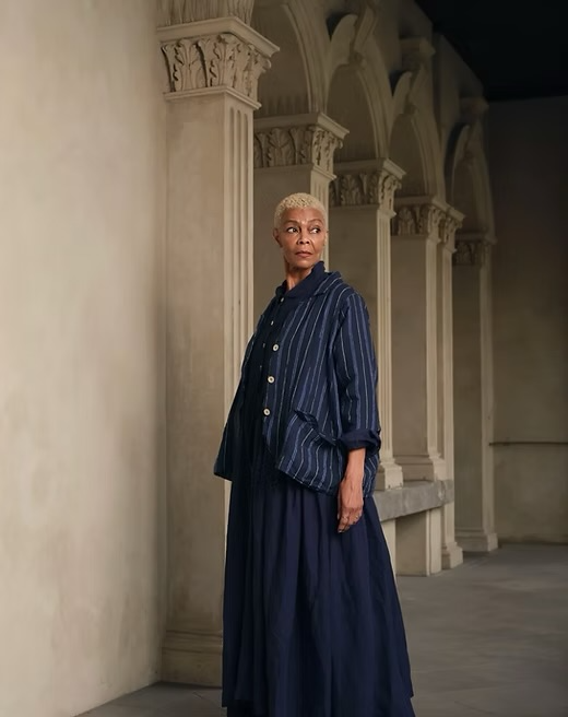 Woman wearing a blue pinstripe linen jacket and flowy matching skirt in an elegant hallway