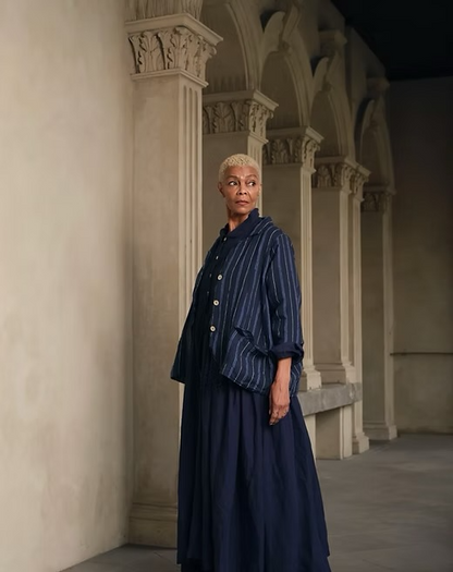 Woman wearing a blue pinstripe linen jacket and flowy matching skirt in an elegant hallway
