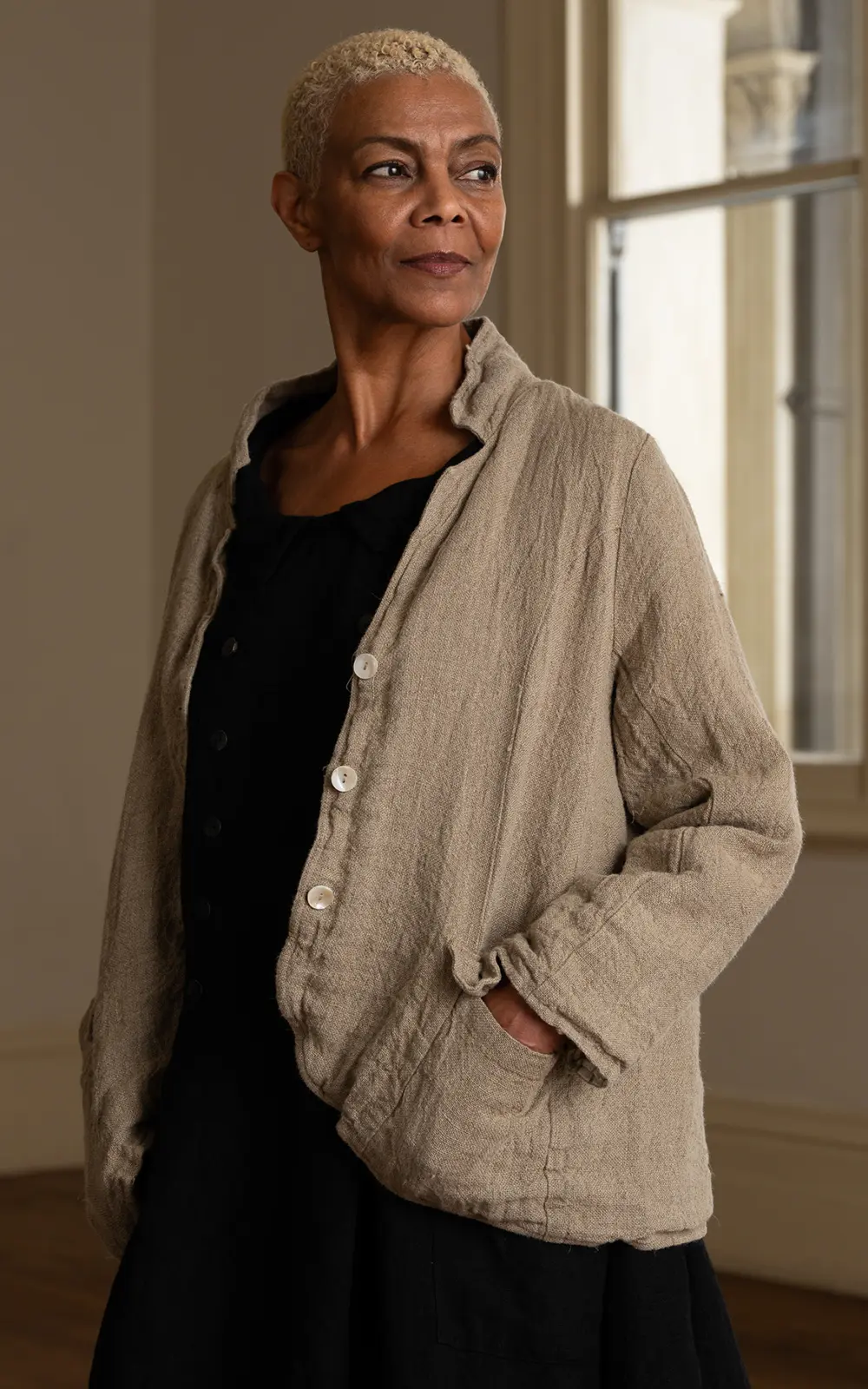 Woman wearing a raw linen jacket with white buttons and pockets indoors