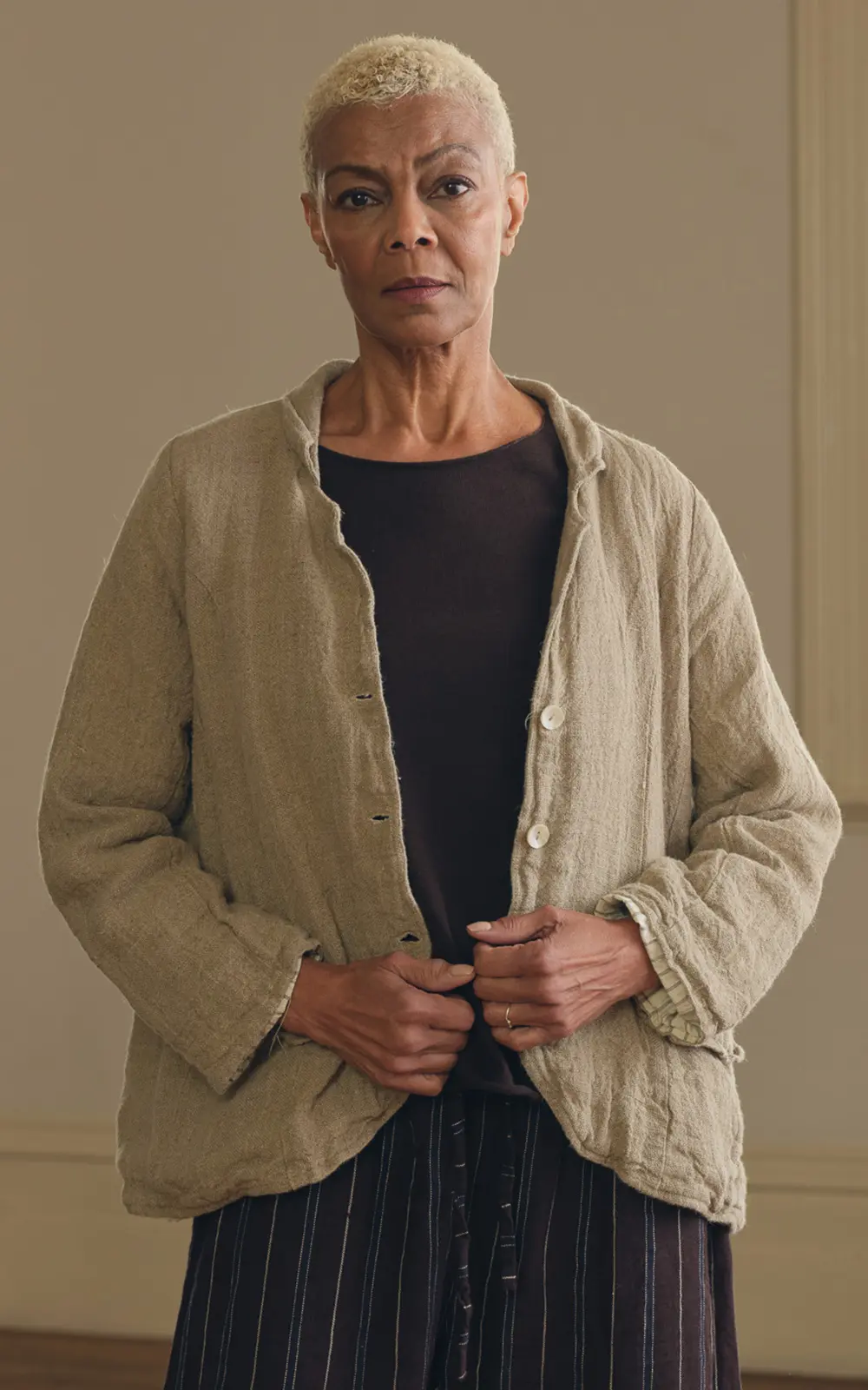 Woman wearing a raw linen jacket over a dark top and striped pants, neutral background