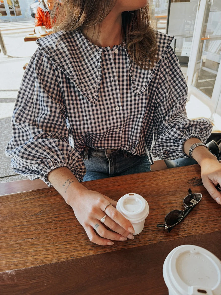 Woman wearing gingham navy shirt with oversized collar featuring a ruffle trim.
