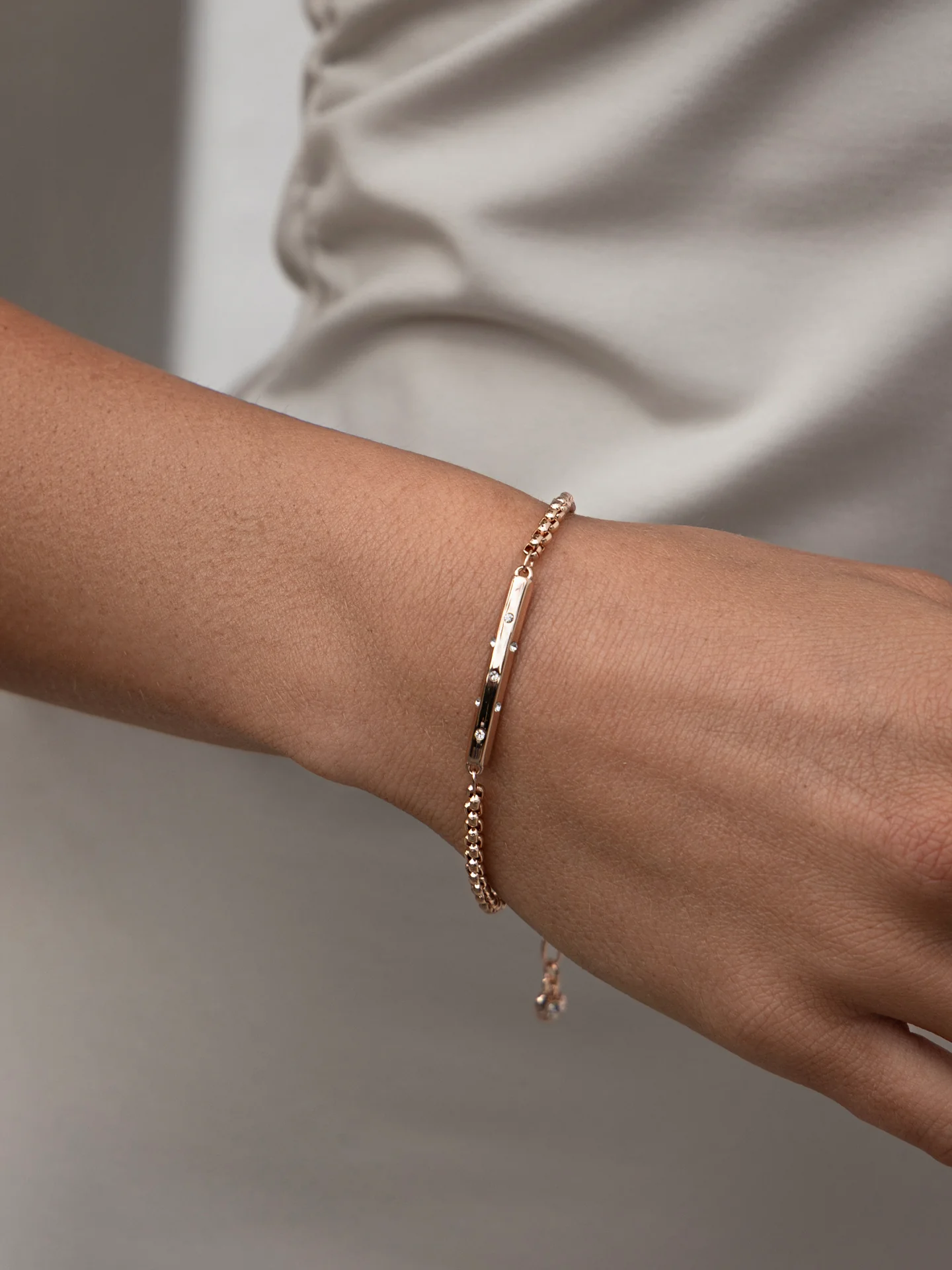 Woman wearing delicate rose gold chain bracelet with bar featuring crystals.