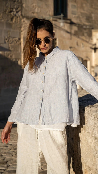 Woman wearing a light blue linen shirt and white linen pants outdoors in sunlight