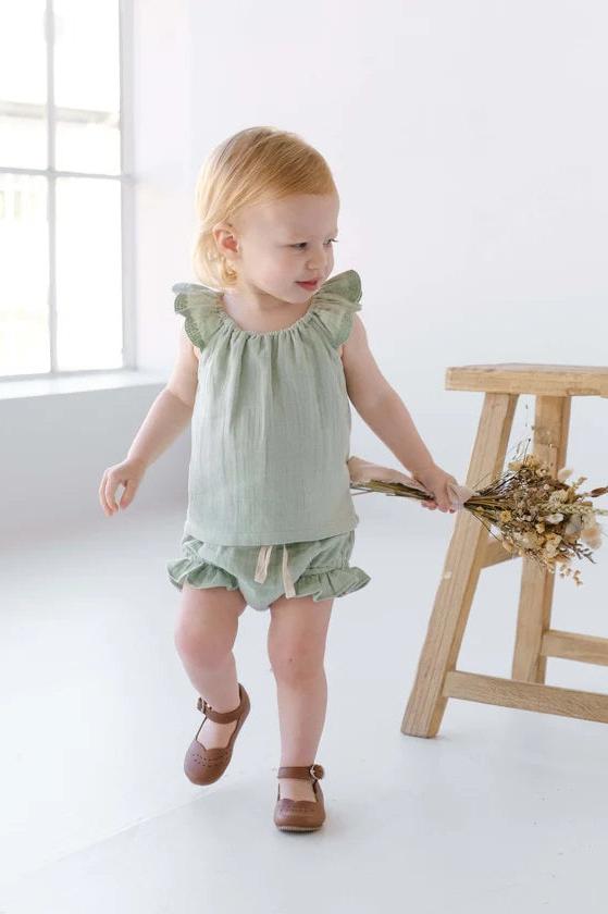 Child wearing sage green ruffle shoulder blouse with bloomer