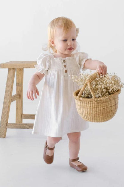 Child wearing white shirred front organic muslin dress with button front