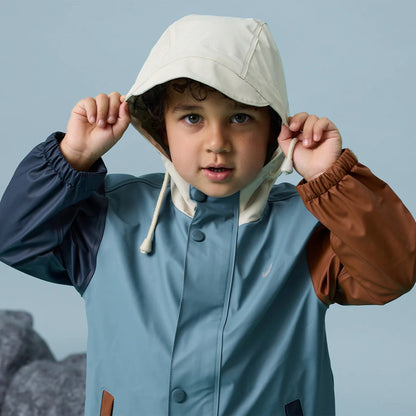 Young boy wearing clock coloured  play jacket in earth and sky colours.