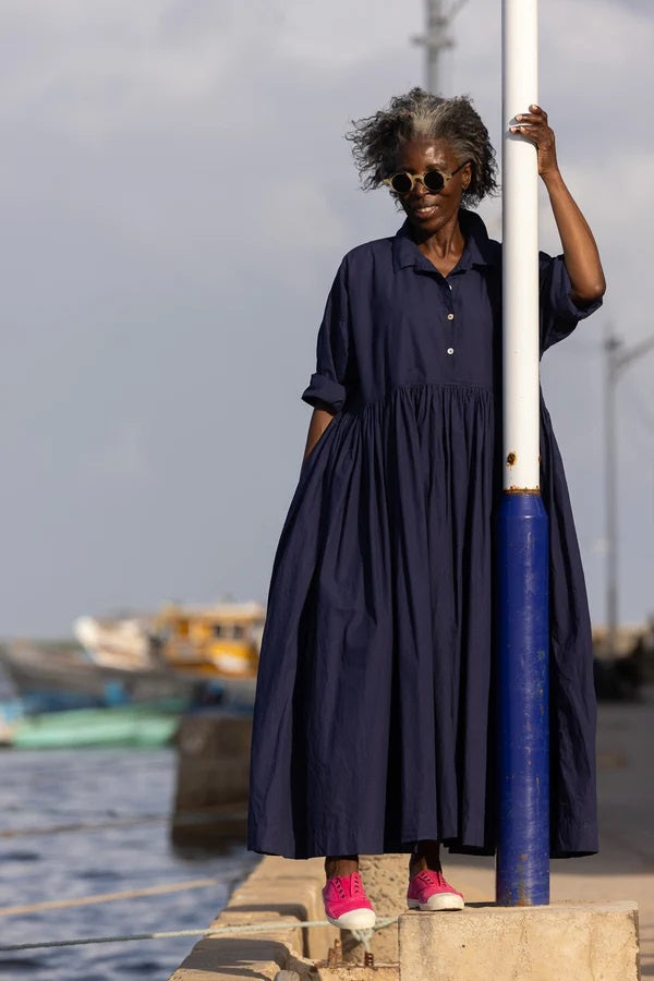 Woman wearing voluminous cotton poplin dress with shirt collar and button down front with shell buttons.