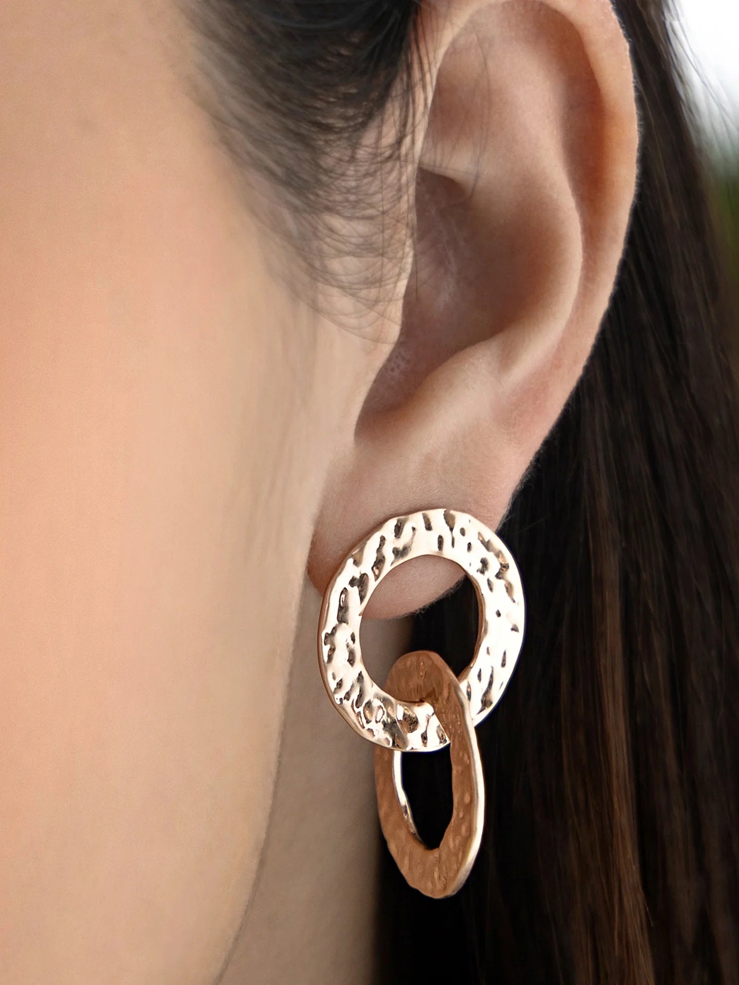 Close-up of a woman's ear wearing gold hammered statement earrings with interlocking circles