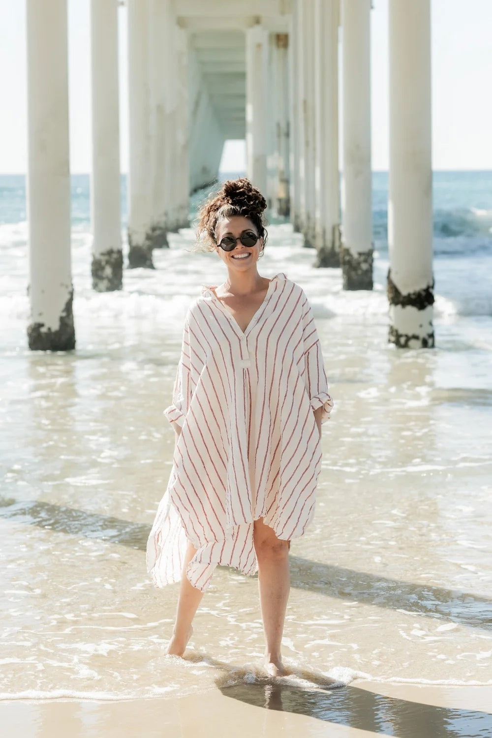 Woman wearing oversize linen shirt dress in red and white stripes.