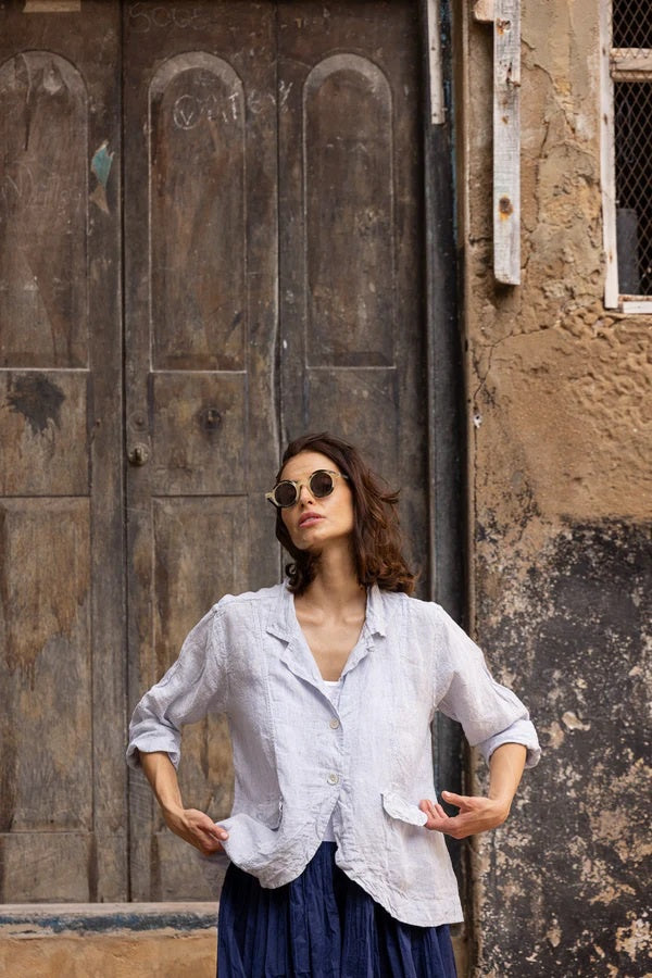 Woman in light linen shirt and dark skirt posing outdoors by rustic wooden door