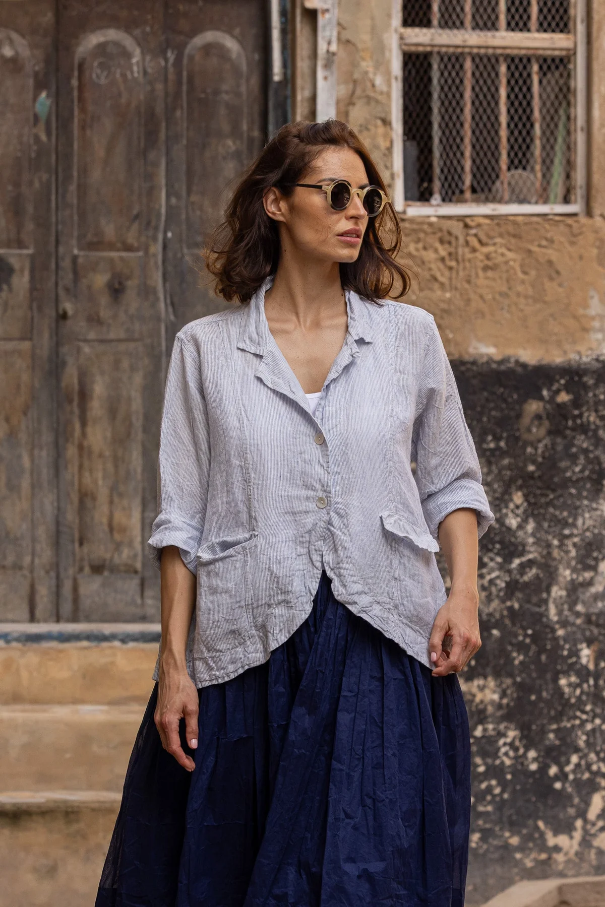 Woman wearing a light linen striped jacket with pockets and navy skirt outdoors