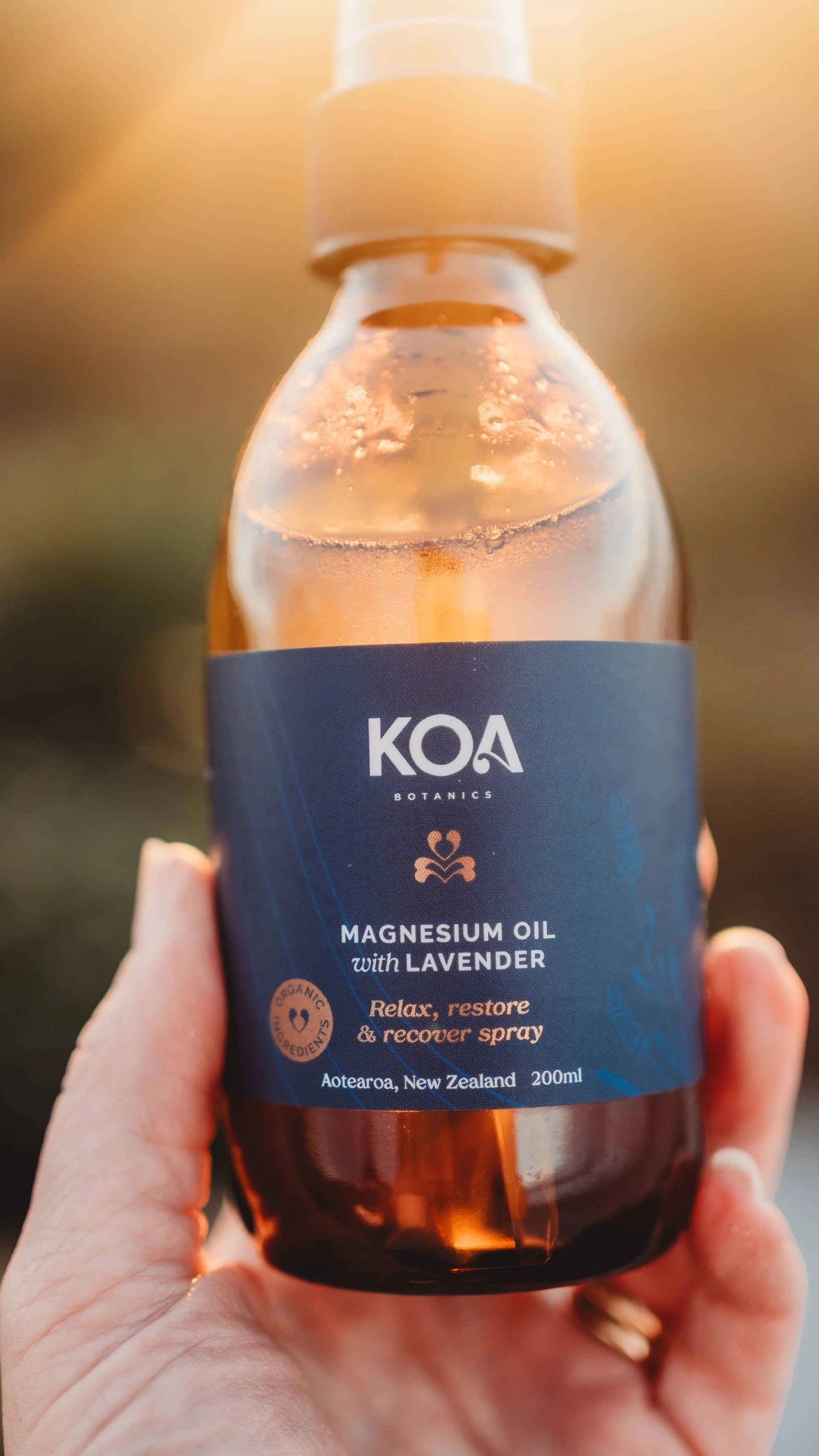 Hand holding a glass bottle of Magnesium Oil and lavender.