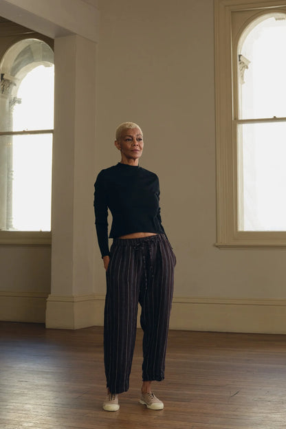 Woman wearing brown striped linen pants and black top standing in a bright, modern room