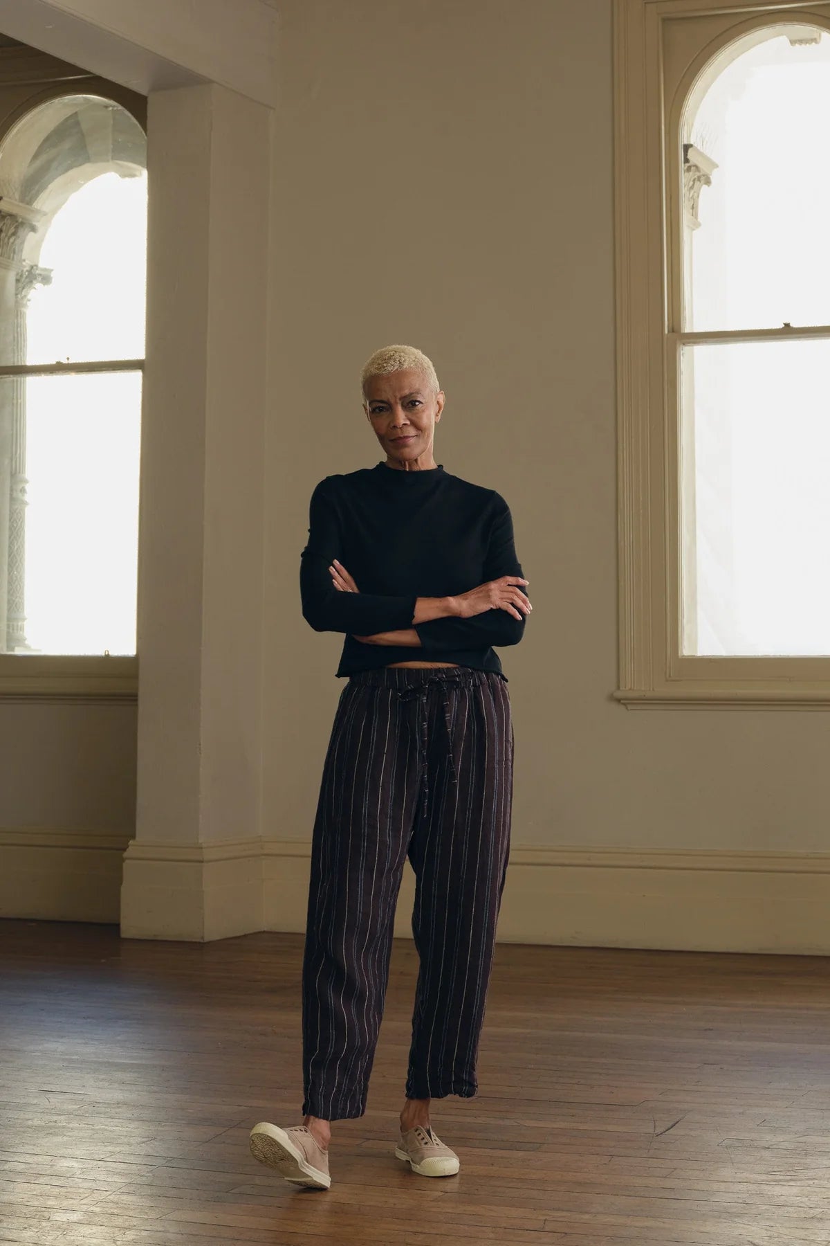 Woman wearing relaxed-fit linen striped pants and black top in a bright room with wood floor