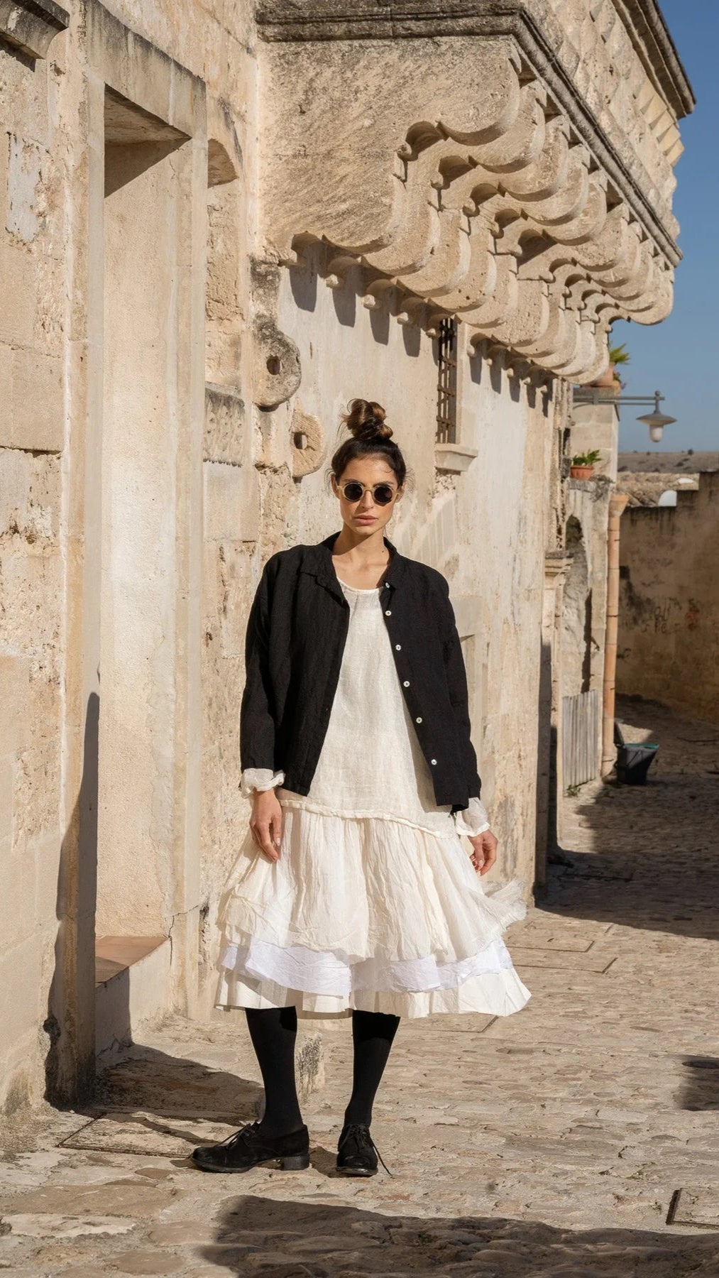 Woman wearing black linen shirt unbottoned layered over dress.