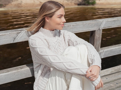 woman sitting down wearing white cable sweater