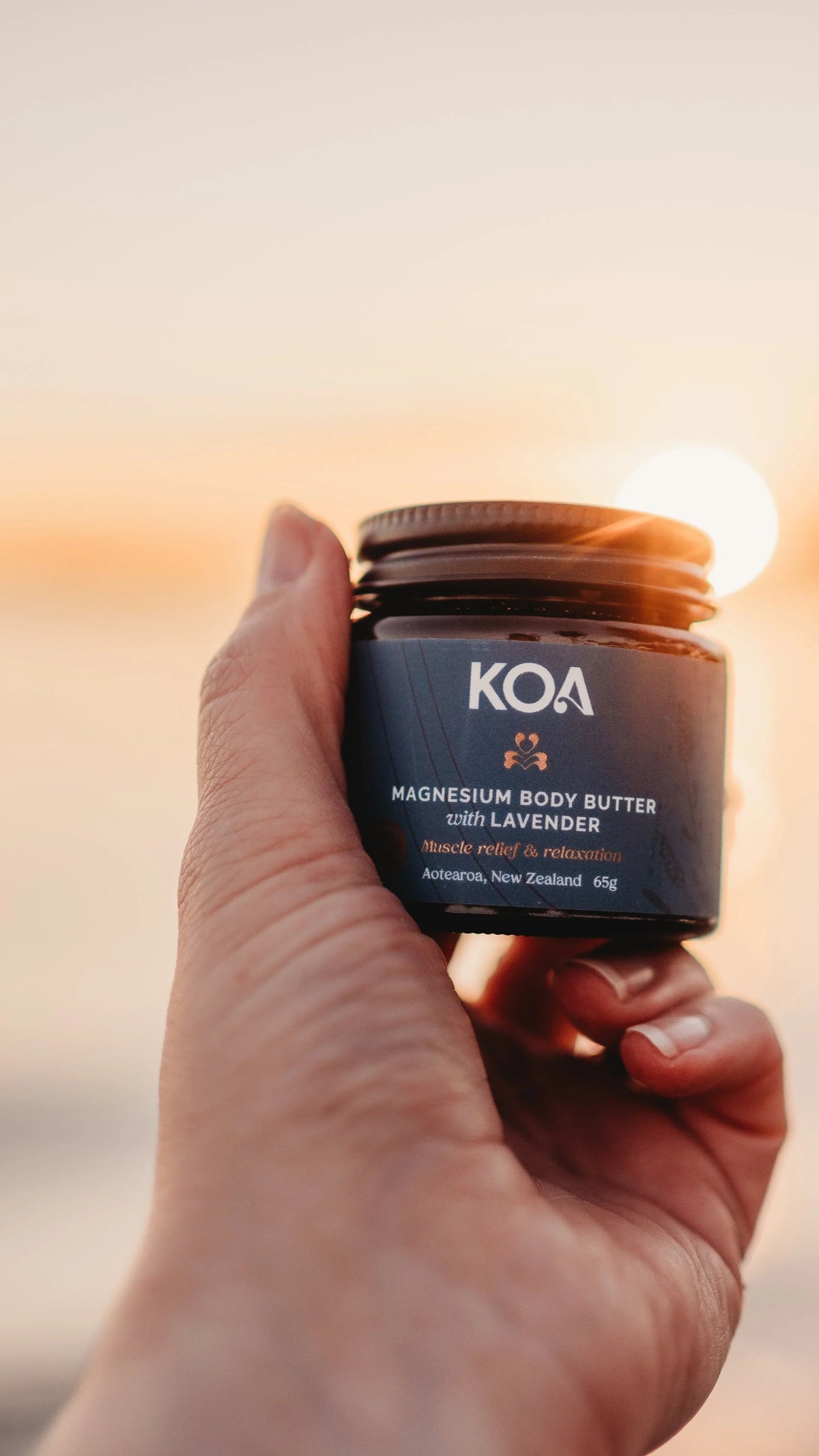 Hand holding KOA magnesium body butter with lavender jar at sunset