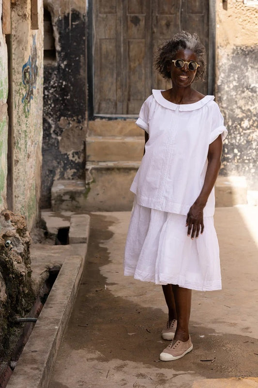 Woman wearing loose cotton white shirt with  front pin tuck detailing, short sleeve and peter pan collar.
