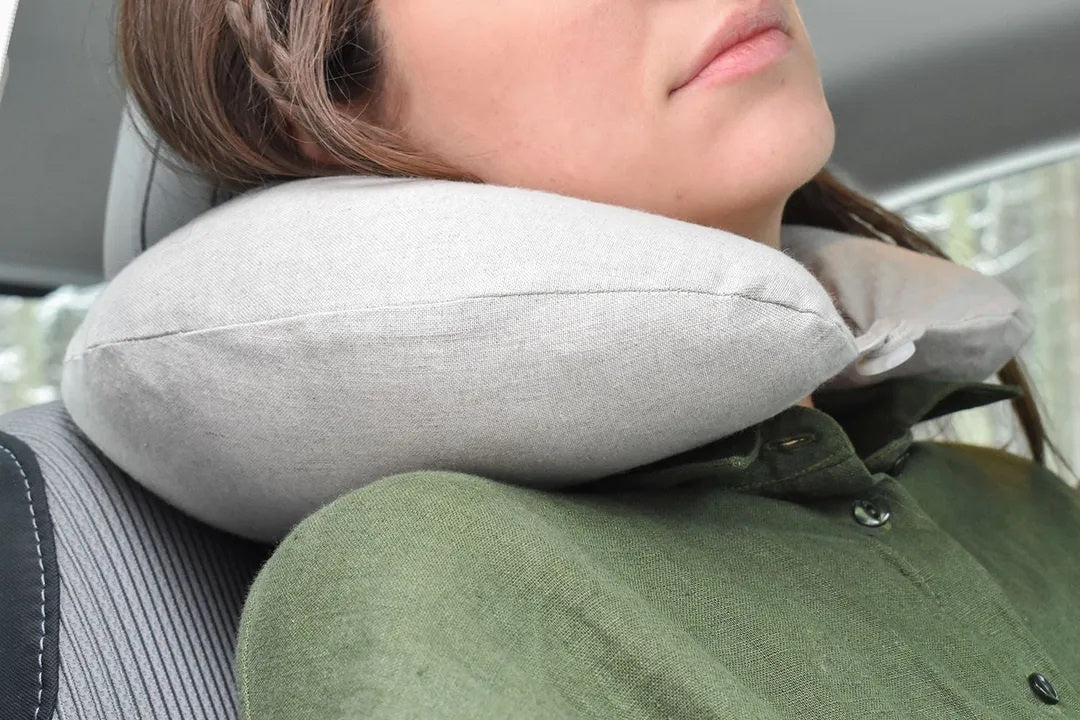 Woman using a light grey linen neck pillow for travel comfort in a car