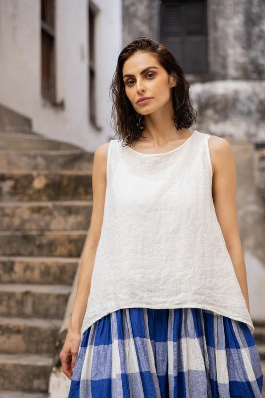 Woman wearing  white linen top, sleeveless with round neck , wide shoulders and tapered sides.