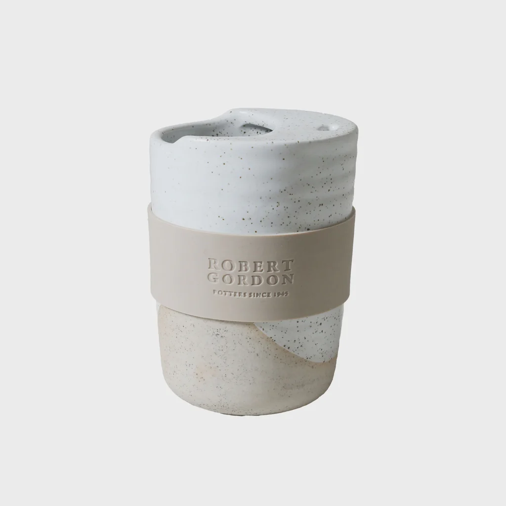 Ceramic travel mug with speckled glaze and beige silicone band on light background