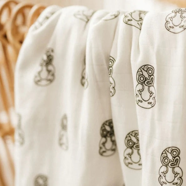 White linen fabric with green Maori-inspired tiki pattern, draped on a chair