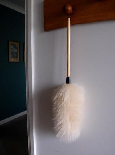 Soft wool duster with wooden handle hanging on wall in home interior