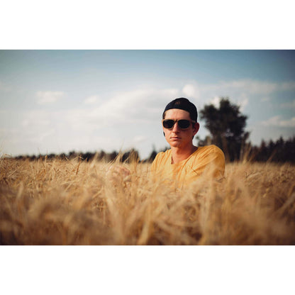 Man in sunglasses and yellow shirt sitting in a wheat field under blue sky