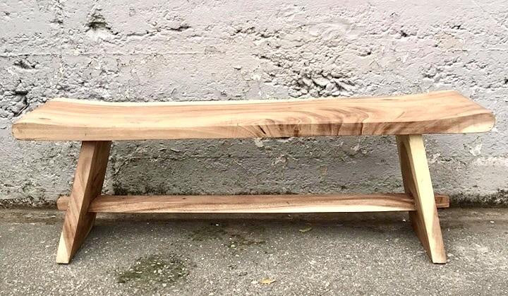 Natural wood bench with angled legs and rustic finish placed against a textured concrete wall