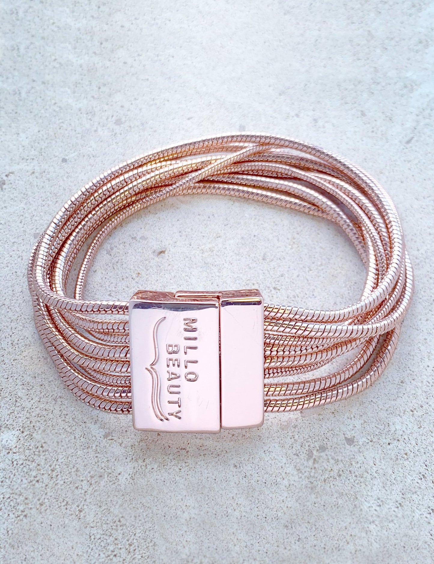 Rose gold multi-strand chain bracelet with engraved clasp on light stone background