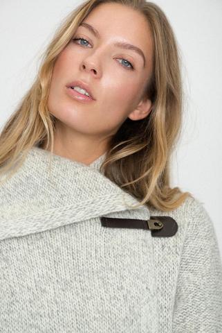 Woman wearing light gray knit sweater with unique buckle neck detail