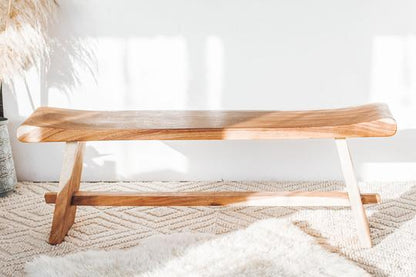 Wooden bench with a natural finish on a textured rug in a sunlit, minimalist room.