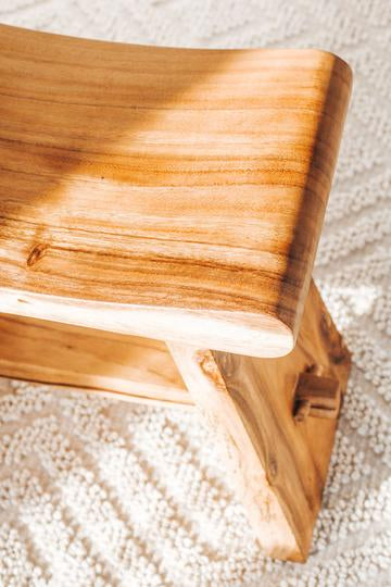 close-up of a wooden bench on a textured cream rug, indoor furniture detail